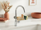 A sink caddy organizer holding soap and sponges on a bright kitchen counter, surrounded by terracotta and burnt sienna decor.